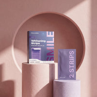 Whitening strips box and a strip pouch on pastel pedestals in front of a blush-pink arch