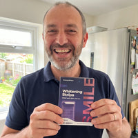 Man smiling in his kitchen holding the whitening strips box