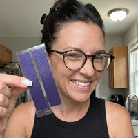 Woman with glasses smiling while holding a tray of whitening strips next to her face